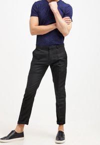 Pantalones negros ajustados con los puños doblados, con una textura de tela suave. Combinados con una camisa de manga corta azul con estampado y zapatillas negras.