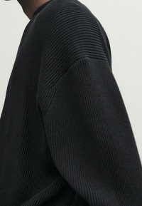 Black ribbed sweater featuring a textured surface, wide sleeves, and a relaxed fit design. Material appears soft and thick.