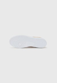 Sola de sapato branca com padrão em grelha e design circular, apresentando o nome da marca Lacoste em relevo no centro.