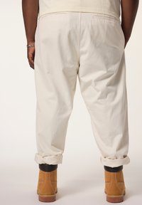 Pantaloni di cotone bianchi con una vestibilità rilassata e orli arrotolati, abbinati a stivali in suede marroni. Presentano due tasche posteriori.
