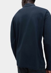 Polo de manga larga en color marino, fabricado en algodón, con un collar clásico y una textura ligera. La vista trasera muestra un corte relajado y detalles en el dobladillo.