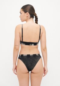 Svart bikiniset med en texturerad bandeauöverdel och högmidjade trosor, accentuerat med kontrasterande sömmar och justerbara axelband.