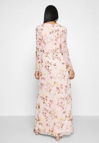 Abito lungo rosa con fiori, maniche lunghe e vita aderente. Presenta un tessuto morbido e fluido con un motivo di fiori gialli e rosa.