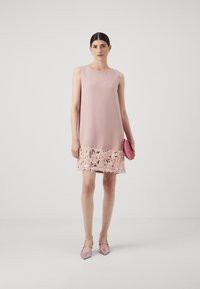 Vestido rosa sem mangas com uma bainha texturizada adornada com lantejoulas. Combinado com uma carteira rosa e sapatos pontiagudos rosa claro. Acabamento em tecido suave.