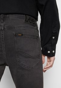 Jeans negros de corte entallado hechos de mezclilla, con un parche de marca en la cintura, costuras sutiles y un diseño clásico de cinco bolsillos.