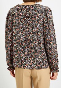 Blusa nera a fiori con fiori rosa, arancio e verdi, scollatura a volant e maniche arricciate con polsini elastici.