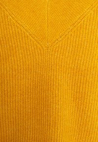Pull en maille jaune présentant un design à col en V, avec une texture côtelée fine et une couleur unie sur toute la surface. Aucun motif ni accent visible.