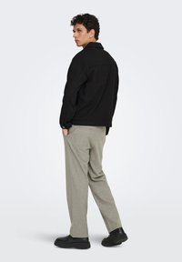 Μαύρο τζιν μπουφάν με γιακά, σε συνδυασμό με ανοιχτό γκρι παντελόνι. Το σύνολο έχει άνετη εφαρμογή και απλές μεταλλικές λεπτομέρειες.