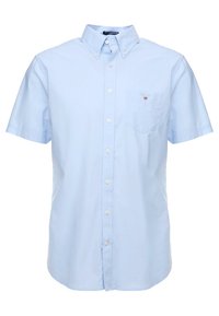 Camisa de botones de manga corta azul claro, material de algodón, con un bolsillo en el pecho, cuello abotonado y un pequeño logo bordado.