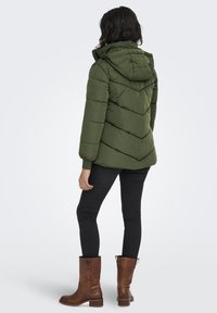 Green puffer jacket with a hood, featuring a chevron pattern, paired with black skinny jeans and brown leather ankle boots.