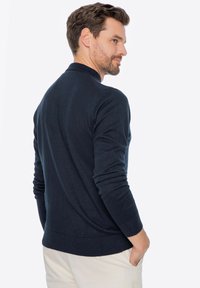 Marineblauer Strickpullover mit geripptem Kragen und Bündchen, in schlanker Passform und glatter Textur, kombiniert mit hellen Hosen.