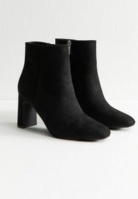 Stivaletti in suede neri alla caviglia con punta affusolata, tacco a blocco e chiusura con zip laterale. Texture liscia con un design minimalista.