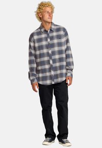 Blauwe en grijze geruite lange mouwen shirt met knopen aan de voorkant, gemaakt van lichte stof; gecombineerd met zwarte broek en kanvas sneakers.