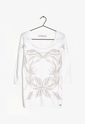 Weißer Pullover mit langen Ärmeln und weitem Ausschnitt, verziert mit metallischen Nietenmustern in Blumenmotiven auf der Vorderseite und gerippten Bündchen.