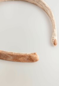 Kergelt beež värviga sametist juukseansambel, millel on sile tekstuur; ümarad otsad mugavuse jaoks ning lihtne, minimalistlik disain.