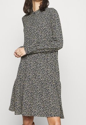 Woman wearing a long-sleeve, knee-length, dark floral dress with a collar and small light-colored flower pattern.