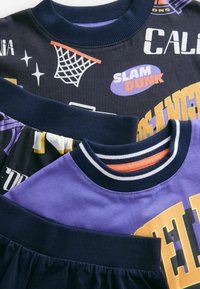 Flerlagrade toppar med mörknavy och lila tyg. Grafiska mönster inkluderar "Slam Dunk" och basketmotiv. Ribbad halsringning.