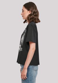 Black short-sleeve t-shirt with a graphic print on the front, relaxed fit, made from cotton, paired with light blue jeans.