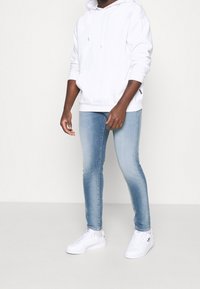 Sudadera blanca con capucha combinada con jeans ajustados de color azul claro y zapatillas blancas. El conjunto presenta un diseño casual yTexturas de tela suaves.