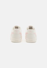 Paire de baskets Puma blanches et rose clair vues de dos, avec le logo Puma sur le talon et la semelle.