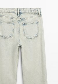 Světle modré džíny z denimu s vybledlým povrchem, které mají dvě zadní kapsy a rovný střih. Textura látky je mírně opotřebovaná.