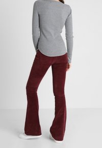 Grå randig långärmad topp i kombination med vinröda hängselbyxor i kordfloret. Byxorna har en slät textur och vanliga bakfickor. Vita sneakers.