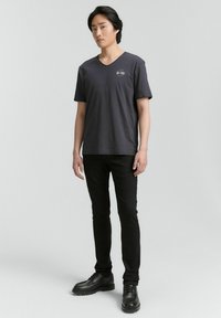Grå v-ringad t-shirt i bomull med korta ärmar. Har en liten logotyp på bröstet. Kombineras med svarta slim-fit byxor och svarta skor.