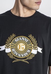 Černé bavlněné tričko s výrazným zlatým a bílým vyšívaným logem s akcenty vavřínu a textem "GIANNI KAVANAGH EST. 2017."