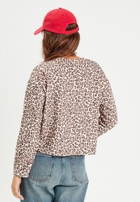 Felpa con stampa leopardata, maniche lunghe, polsini a costine e vestibilità corta. Abbinata a jeans in denim blu a vita alta e un cappellino rosso.