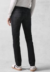 Zwarte denim jeans met een slim fit, twee achterzakken en een gladde textuur. Gecombineerd met een grijze trui en casual schoeisel.