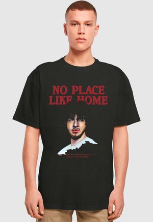 Sort bomulds t-shirt med et iøjnefaldende grafisk print af en persons portræt, med teksten "INGEN STED SOM HJEM" ovenfor og "JACK HARLOW" nedenfor.