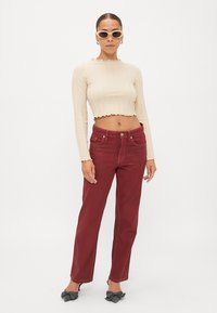 Beige ribbet crop top med bølget kant, parret med højtaljede, lige burgunder jeans. Sorte sko med sløjfedetalje. Hvide solbriller.