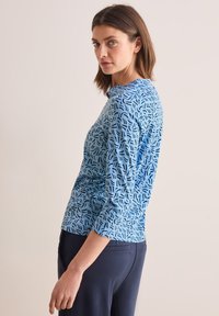 Blauwe langoeve shirt met een gemustreerd ontwerp met zwarte lijnen, ronde halslijn en een aansluitende pasvorm, gecombineerd met donkere broek.