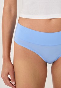 Bas de bikini bleu clair en tissu extensible, avec une large taille et une texture lisse sans motifs ni embellissements visibles.