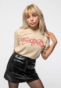 Beige cotton t-shirt with red logo, paired with a high-waisted black patent leather mini skirt. Smooth texture, fitted design.