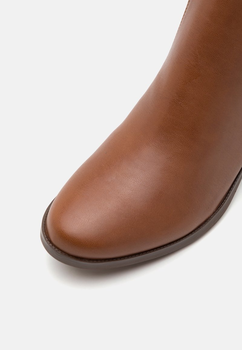 Bottine en cuir marron avec un bout arrondi, texture lisse et un éclat subtil. Les coutures le long de la semelle ajoutent une finition raffinée.