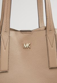 Sac à main en cuir beige texturé avec deux anses et un petit logo MK doré centré près du haut.