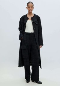 Zwarte tweed lange jas met rafelige randen, gecombineerd met bijpassende broek met een ruitpatroon en een witte tanktop; elegante op maat gemaakte stijl.