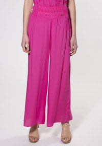 Pantaloni a gamba larga rosa realizzati in tessuto leggero con una vita testurizzata. Presentano un dettaglio del marchio discreto sulla vita.