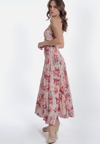Abito maxi floreale in rosa, con bustino arricciato, gonna a livelli e materiale fluido. Abbinato a sandali con zeppa beige.