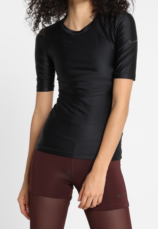 Femme portant un haut de sport noir ajusté à manches courtes et un short de sport bordeaux taille haute avec des leggings transparents dessous.