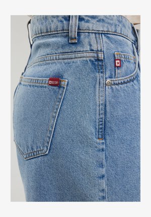 Heledad sinine denim teksad, millel on kulunud viimistlus. Tagataskul on punane silt, oranž õmblus ja klassikaline viie-tasku disain.