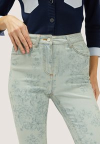 Jeans de mezclilla azul claro con estampado floral, diseño de cintura alta y costuras en contraste. Cuenta con un bolsillo frontal y cierre de botón.