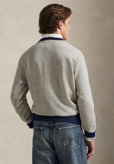 Gray sweatshirt with navy ribbed cuffs and hem, textured fabric, and a crew neckline, paired with blue denim jeans.