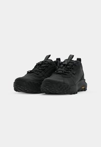 Black athletic shoes with a textured upper, reinforced toe, and aggressive tread pattern. Features elastic laces and pull tabs. Vibram logo visible.