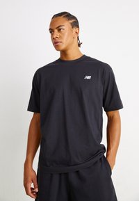 Black short-sleeve t-shirt in a relaxed fit, featuring a small white New Balance logo on the left chest. Smooth cotton material.