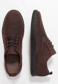 Hnědé boty z semiše s kulatou špičkou, zavazováním na tkaničky, kontrastním prošitím a černou gumovou podrážkou. Čistý, moderní tvar s jemnými detaily.