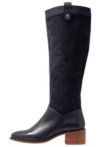 Knähöga stövlar i marinblå mocka med en slät lädertå och häl. Har en rund tå, blockklack i trä och ett rem vid toppen.