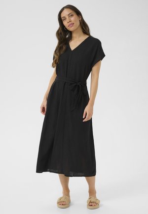Schwarzes Leinen-Maxikleid mit kurzen Ärmeln, V-Ausschnitt und Taillenband. Glatte Textur mit lockerer Passform, kombiniert mit geknoteten Sandalen.