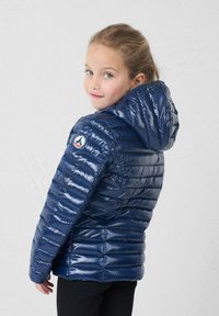 Marineblauwe pufferjack met capuchon, met een glanzende, geplooide textuur en een logo patch op de schouder. Ontworpen voor kinderen.